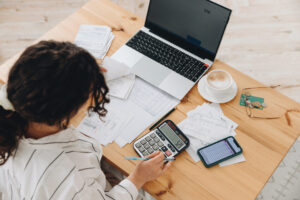 Woman looking down at a calculator, laptop, and papers