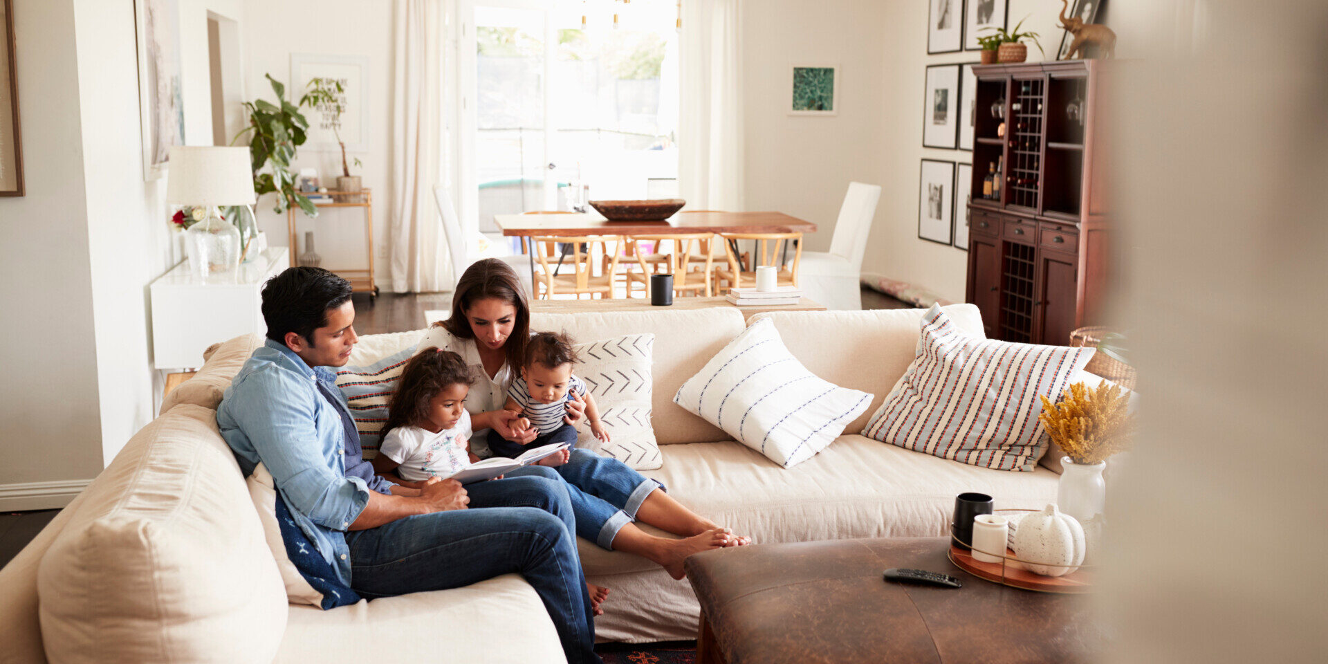 Young Sitting On Sofa Reading A Book Together In The Living Room, Seen From Doorway